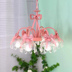 Front view of a pink multi-arm chandelier featuring pink bows, crystal pendants, and clear glass shades, with greenery in the background.