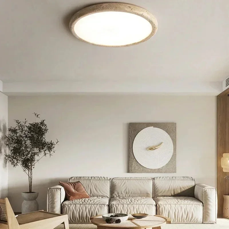 A circular flush mount ceiling light with a textured, stone-like beige frame and a smooth white diffuser, installed in a modern living room above a sofa.