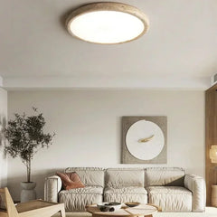 A circular flush mount ceiling light with a textured, stone-like beige frame and a smooth white diffuser, installed in a modern living room above a sofa.