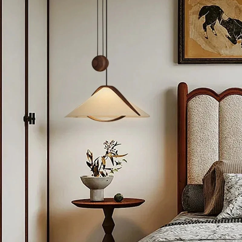Fabric cone pendant light with wood trim hanging above a bedside table.