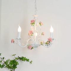 View of a white iron chandelier with pink roses and green leaves, featuring a central bowl and candle-style lights.