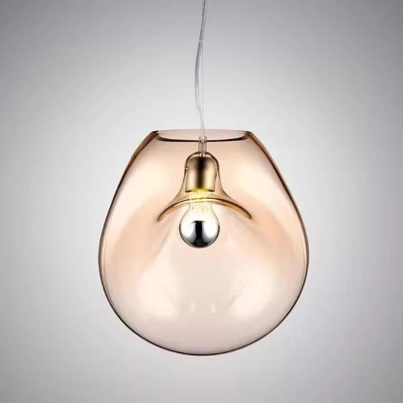 Amber glass organic shape pendant light with a visible bulb and cord, against a gray background.
