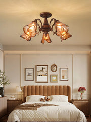 A semi-flush mount ceiling light with a brushed bronze finish and five amber stained glass shades arranged in a floral pattern, illuminating a bedroom.