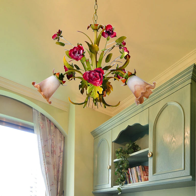 A gold floral chandelier with red rose buds and frosted glass shades, partially obscured by a window curtain.