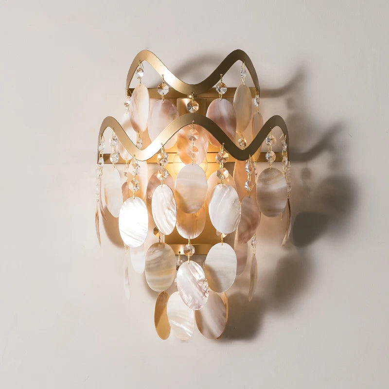 Gold wavy wall sconce with cascading shell and crystal embellishments against a white wall.
