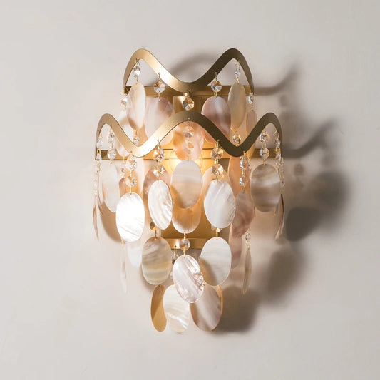 Gold wavy wall sconce with cascading shell and crystal embellishments against a white wall.