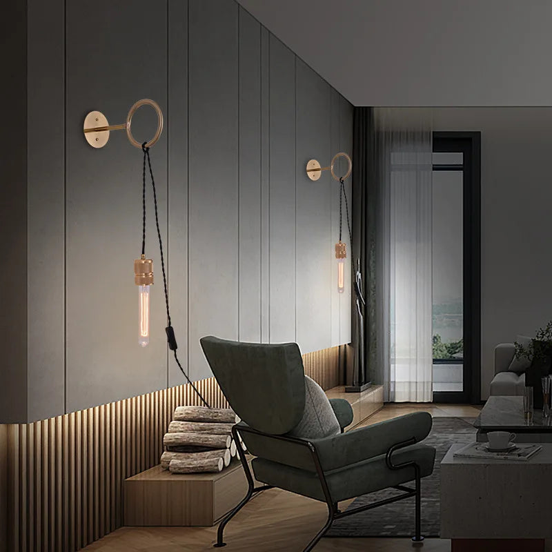 Two gold ring wall sconces illuminating a modern living room with a chair and fireplace.