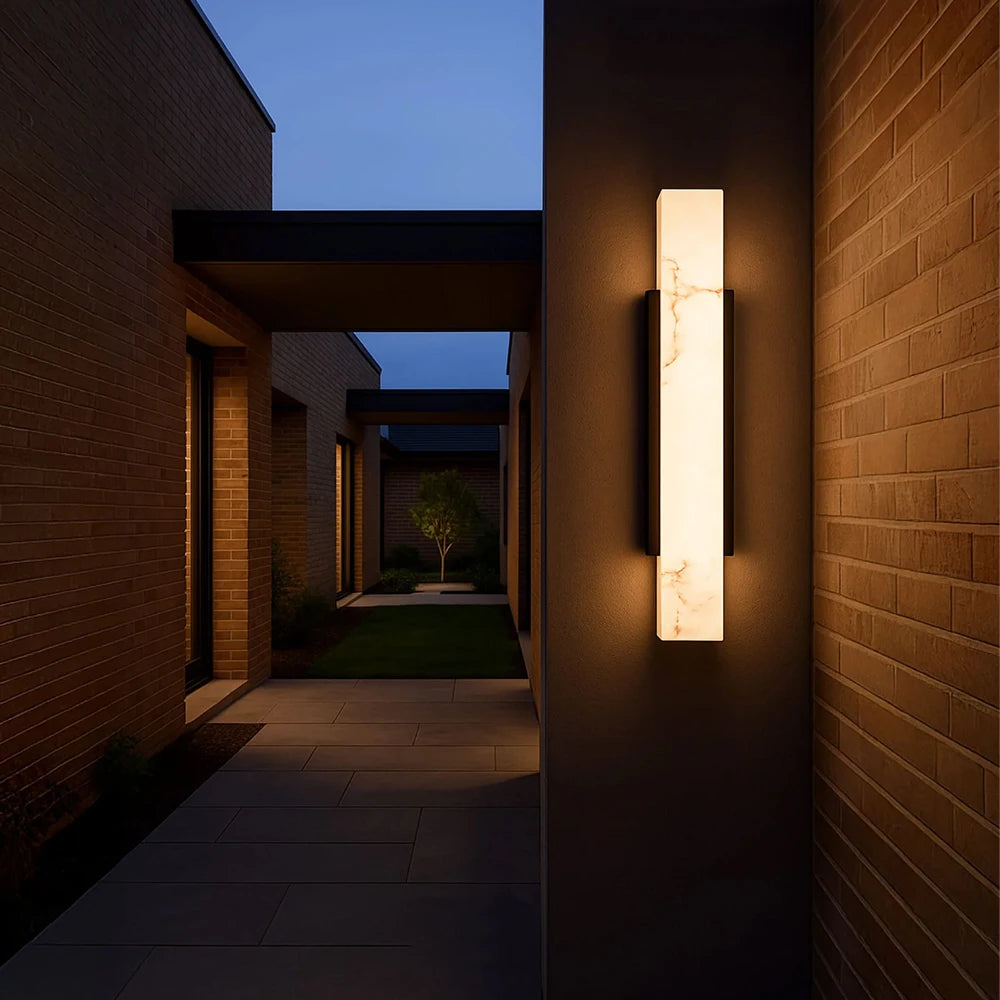 A dark brick walkway illuminated by a modern wall sconce with a marble-effect diffuser.
