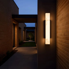A dark brick walkway illuminated by a modern wall sconce with a marble-effect diffuser.