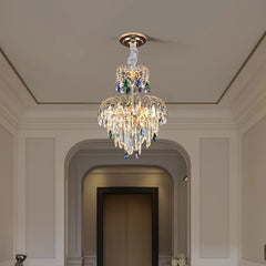 A gold multi-tier crystal chandelier in a well-lit hallway with an arched doorway in the background.