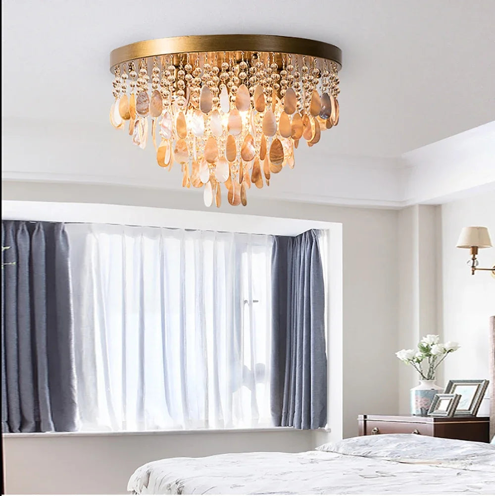 A gold and shell semi-flush mount ceiling light with multiple tiers of teardrop shapes hanging from a circular base, above a bed in a bedroom.
