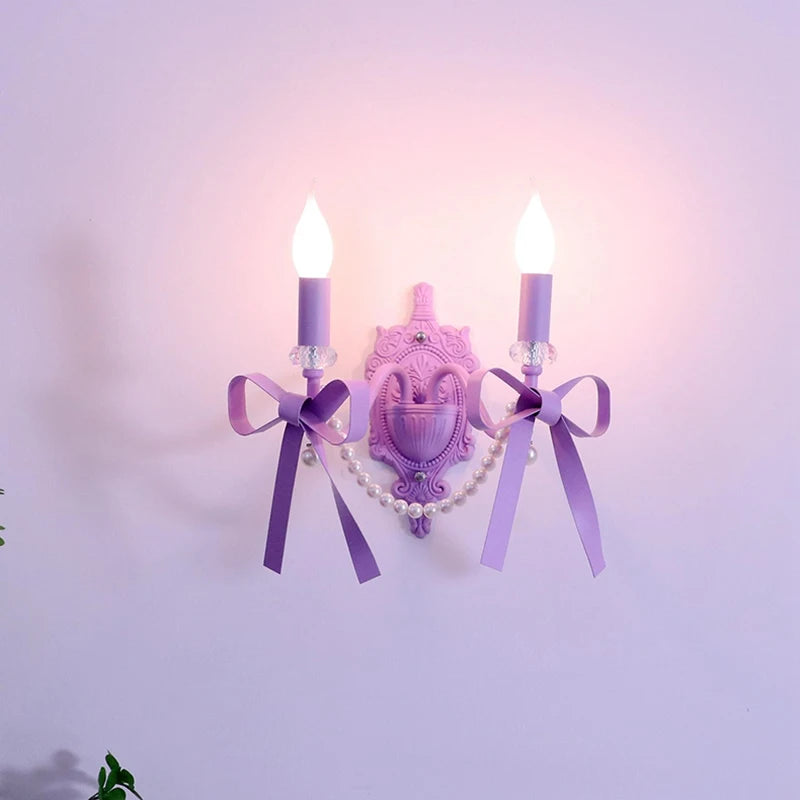 Close-up view of a purple wall sconce featuring two candle-style lights, ornate detailing, and decorative purple bows.