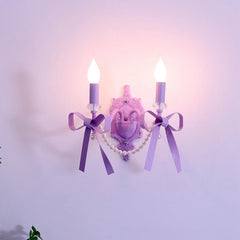 Close-up view of a purple wall sconce featuring two candle-style lights, ornate detailing, and decorative purple bows.