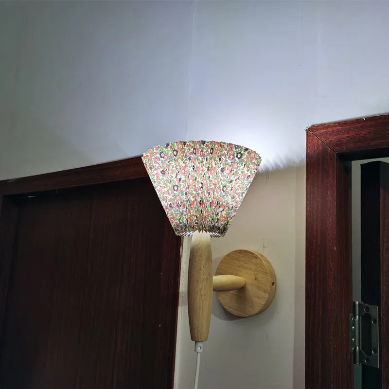 Wall-mounted lamp with floral-patterned shade and wooden base on a white wall.