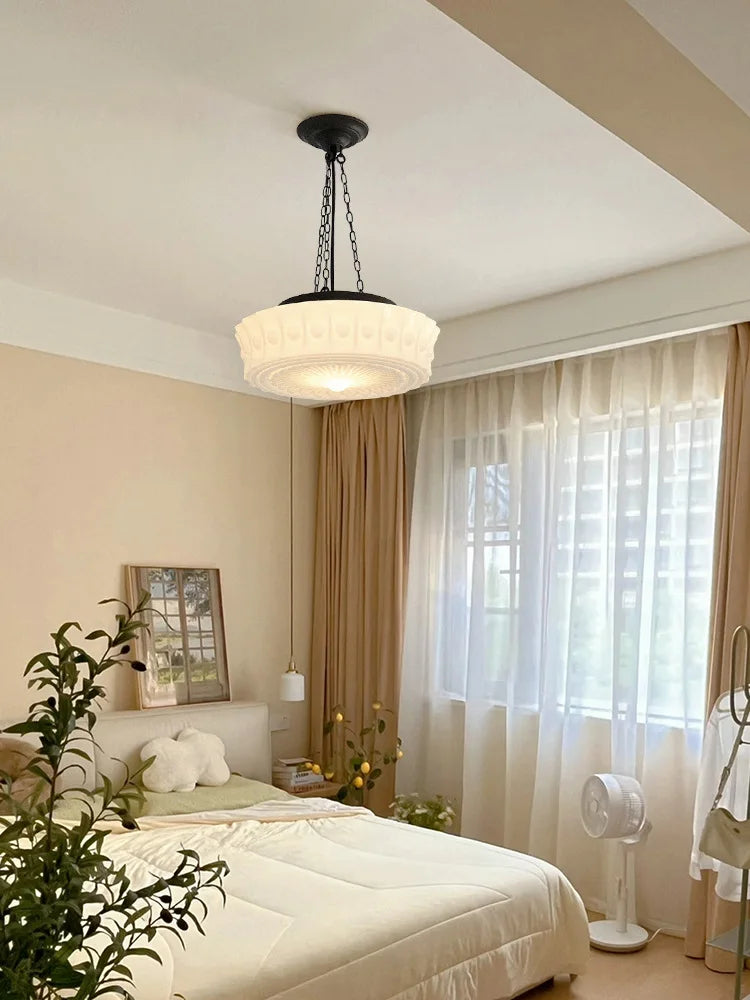 Cream decorative glass pendant light with a black chain hanging in a bedroom above a bed.