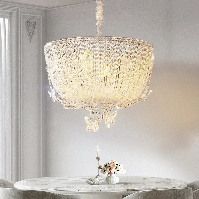 A luxurious polished chrome crystal waterfall pendant light with many crystal strands hanging over a marble-top dining table.