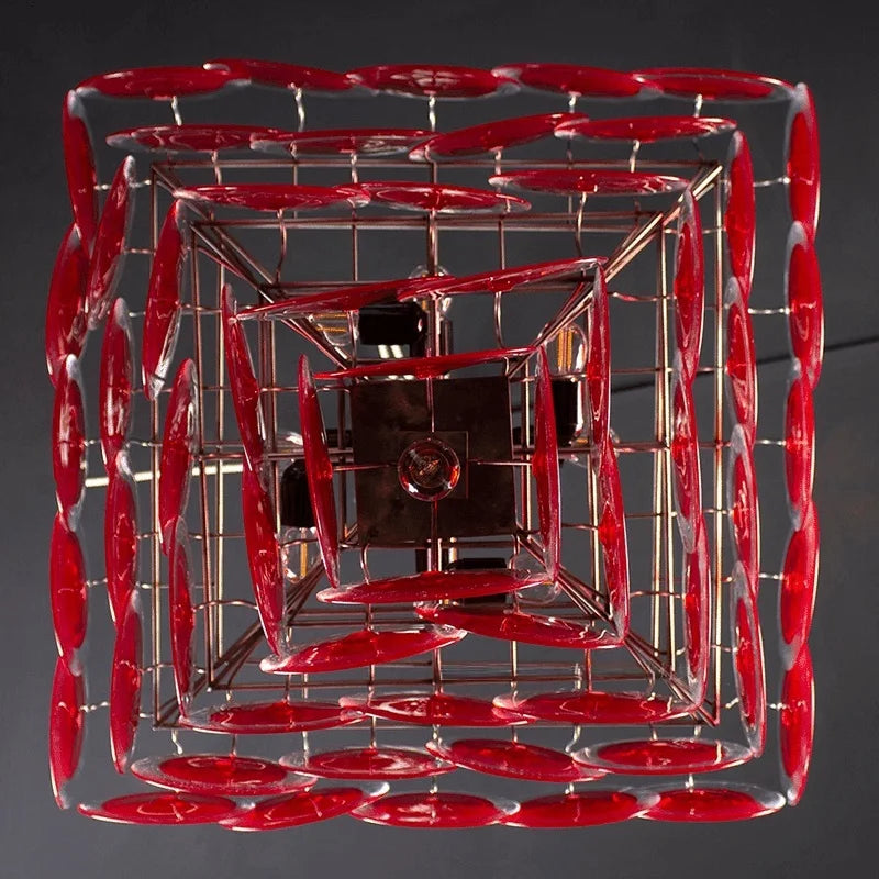 A tiered red glass chandelier hanging in a dimly lit room, casting a warm glow.