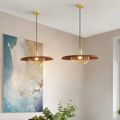 Two wood-finish pendant lights with gold cages hanging above a dining table.