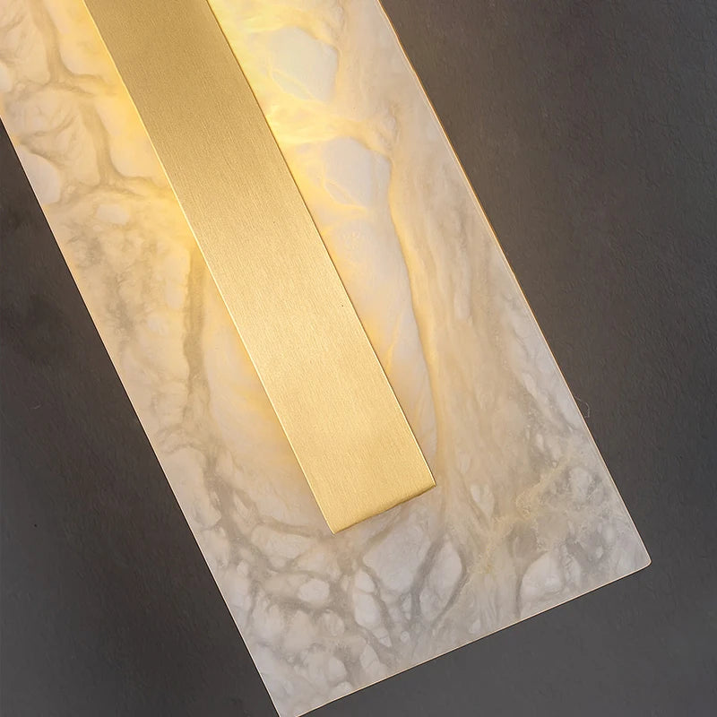 Gold rectangular light fixture on a marble surface with a dark background