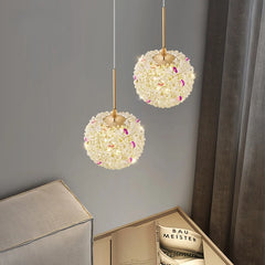 Two gold crystal orb pendant lights hanging in a room with curtains and a shelf.