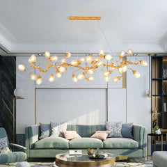 A long, horizontal gold chandelier with a branch-like design and numerous clear, fruit-shaped glass globes hangs above a light green sofa in a modern living room.