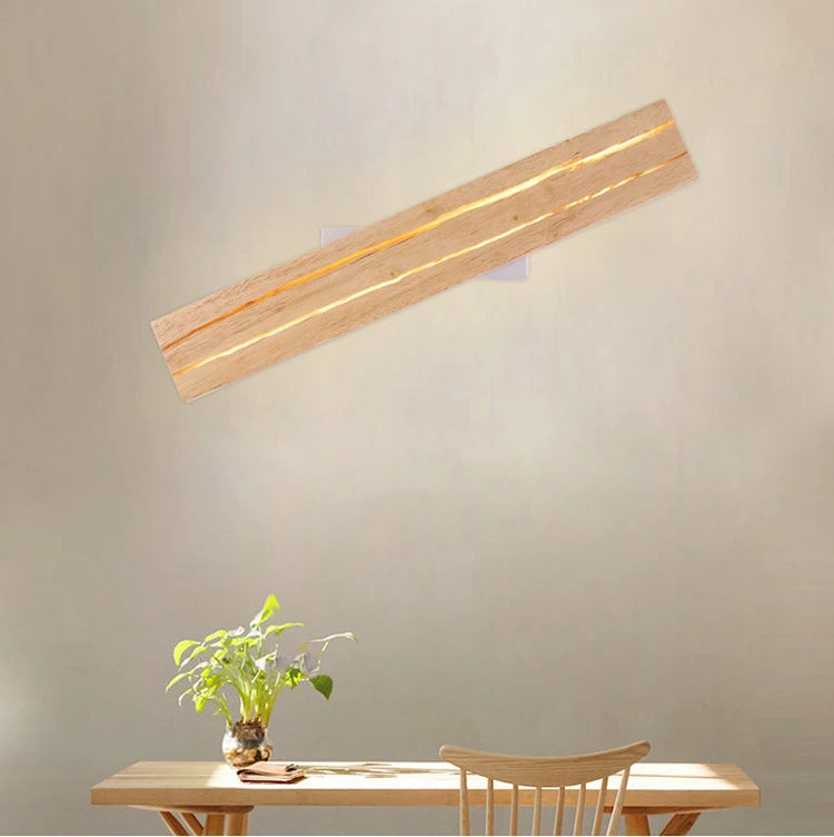 Wooden wall lamp on a plain wall with a table and plant in the foreground