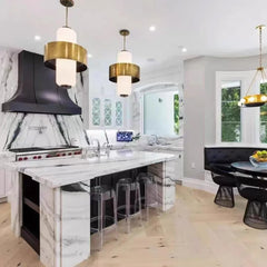 A spacious kitchen with a marble island, black range hood, and pendant lights.
