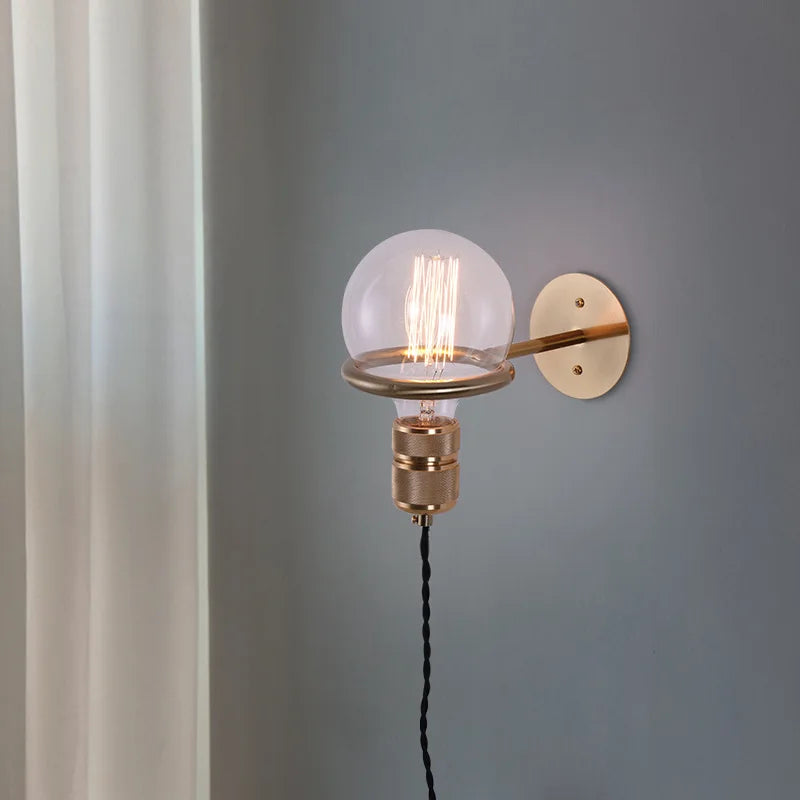 Gold ring and clear glass shade on a wall-mounted pendant light with a visible filament LED bulb.