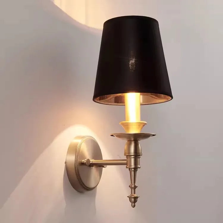 Wall-mounted lamp with black shade and brass base on a light gray background