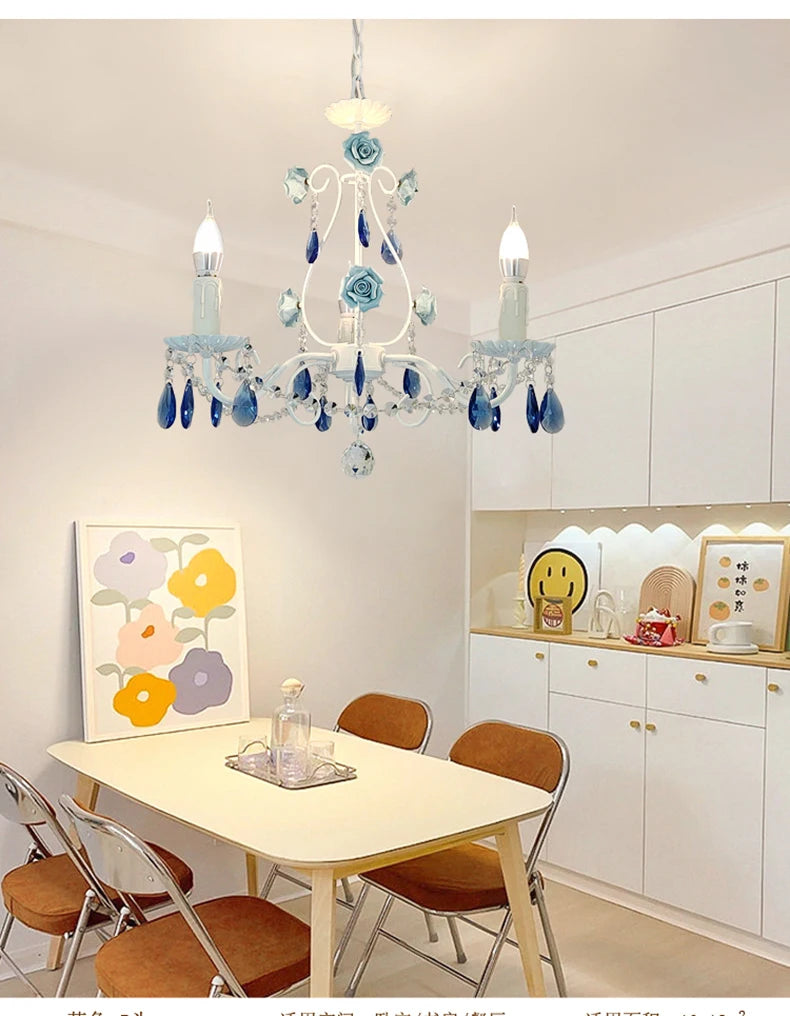 White floral crystal chandelier illuminated above a dining table with chairs in a bright room with white cabinets.