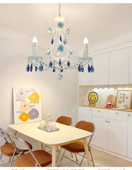 White floral crystal chandelier illuminated above a dining table with chairs in a bright room with white cabinets.