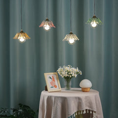 A round table with a vase of flowers and a framed picture, with four colorful glass pendant lights hanging in the background.