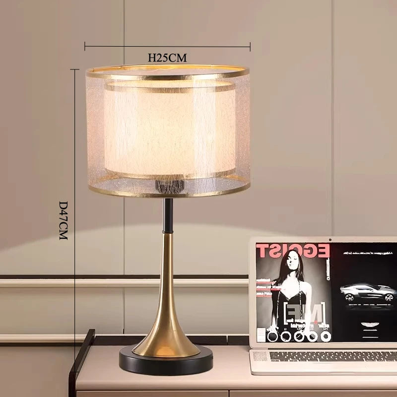 Gold table lamp on a desk with a magazine and laptop, dimensions displayed.