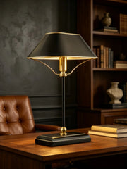 Black metal table lamp with a polished chrome finish and a cone-shaped shade, casting light upwards and downwards, placed on a wooden desk.