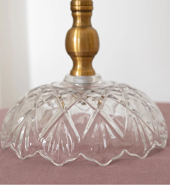 Clear glass lampshade with a brass base on a pink surface.