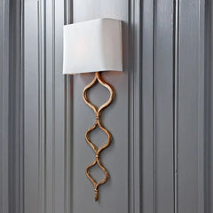 A gold wall sconce with a quatrefoil chain and fabric shade mounted on a dark gray paneled wall.