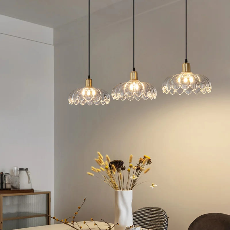 A dining table setting with three hanging pendant lights, each with a gold base and floral glass shade, creating ambient lighting.