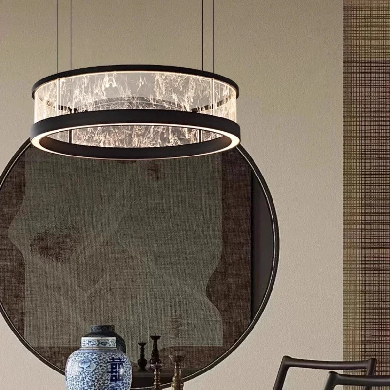 A black ring pendant light with a textured glass diffuser, positioned in front of a large decorative circular tapestry and a blue and white ceramic vase.
