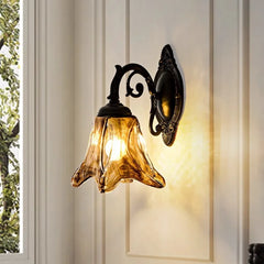 A single bronze glass bell wall sconce mounted on a cream-colored wall, with a window and greenery visible to the left.