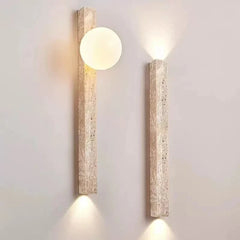 Two travertine stone wall sconces mounted on a plain wall, one with a frosted globe and warm light.