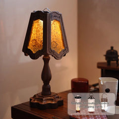 Close-up of a table lamp with a patterned glass shade and a dark wood base, emitting a warm yellow light.