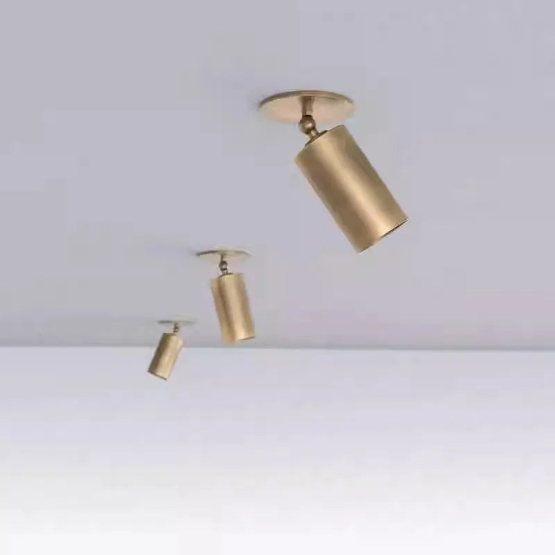 Three brushed brass cylinder spotlights of varying sizes mounted on a white ceiling, arranged diagonally.