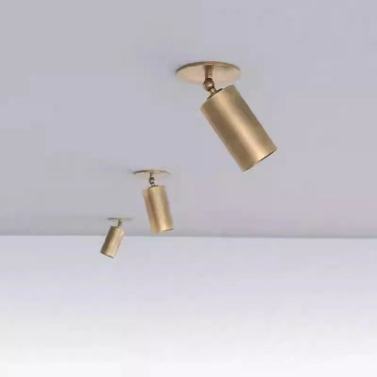 Three brushed brass cylinder spotlights of varying sizes mounted on a white ceiling, arranged diagonally.