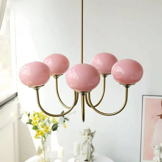 A gold chandelier with five pink globe-shaped glass shades, positioned above a white table.