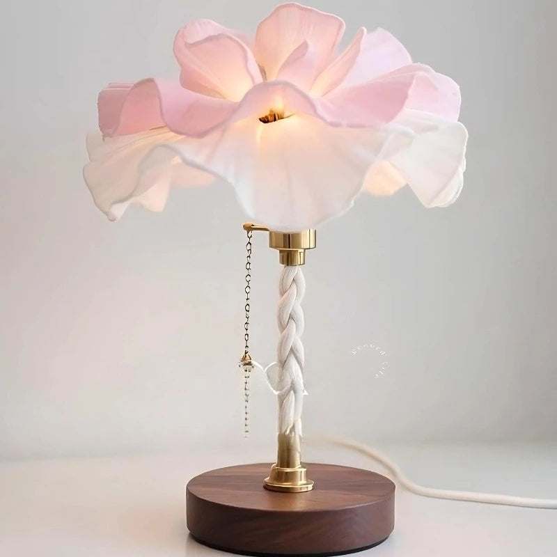 A close-up view of a white and pink petal-shaped table lamp with a brushed nickel base and pull chain.