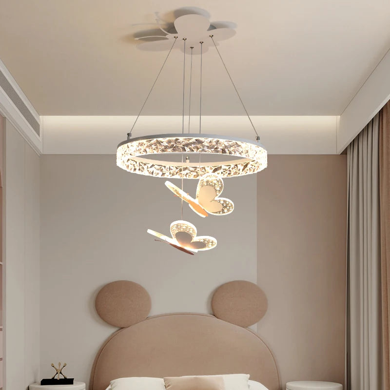 A close-up of a crystal ring pendant light with butterfly accents, hanging in a softly lit bedroom.