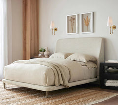 Beige upholstered bed in a bedroom setting with side tables and wall decor.