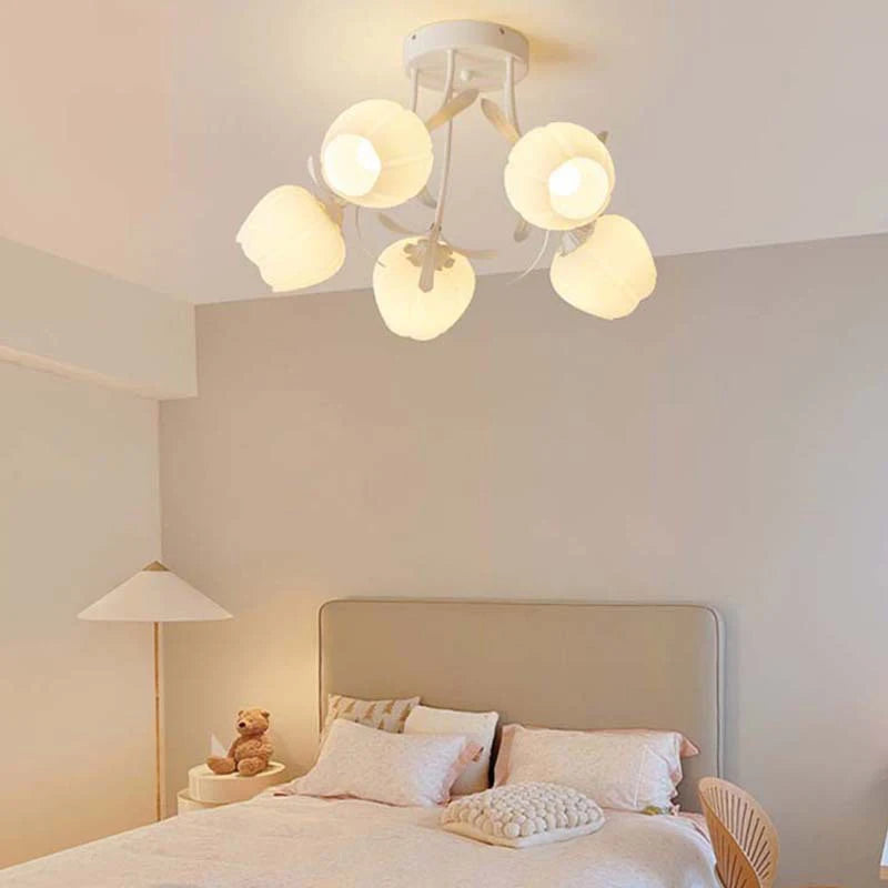 A bedroom scene with a white semi-flush mount light fixture with five flower-shaped shades, illuminating a bed and nightstand.