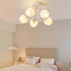A bedroom scene with a white semi-flush mount light fixture with five flower-shaped shades, illuminating a bed and nightstand.