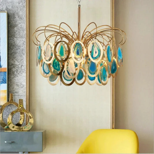 A close-up of a gold chandelier featuring oval-shaped, colorful agate slices suspended within gold rings.